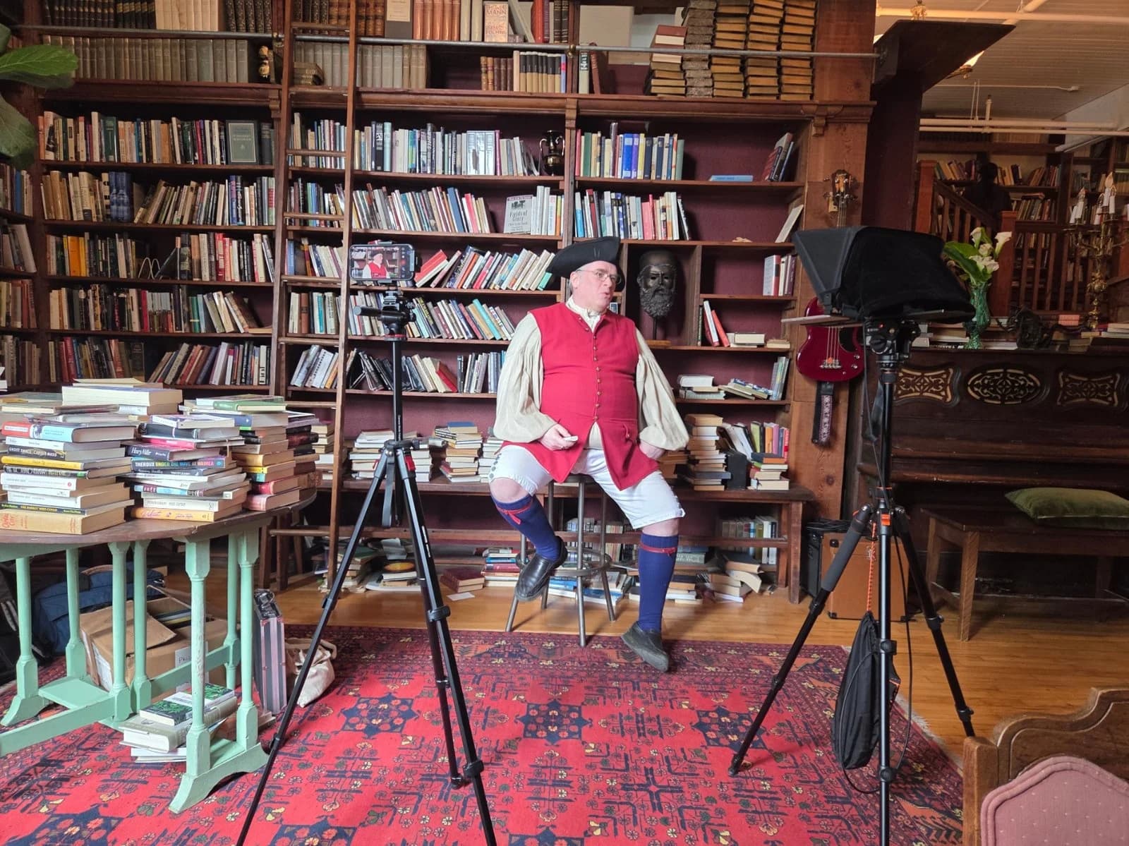 Author being professionally filmed in a library setting with cameras, lighting equipment, and a large collection of books